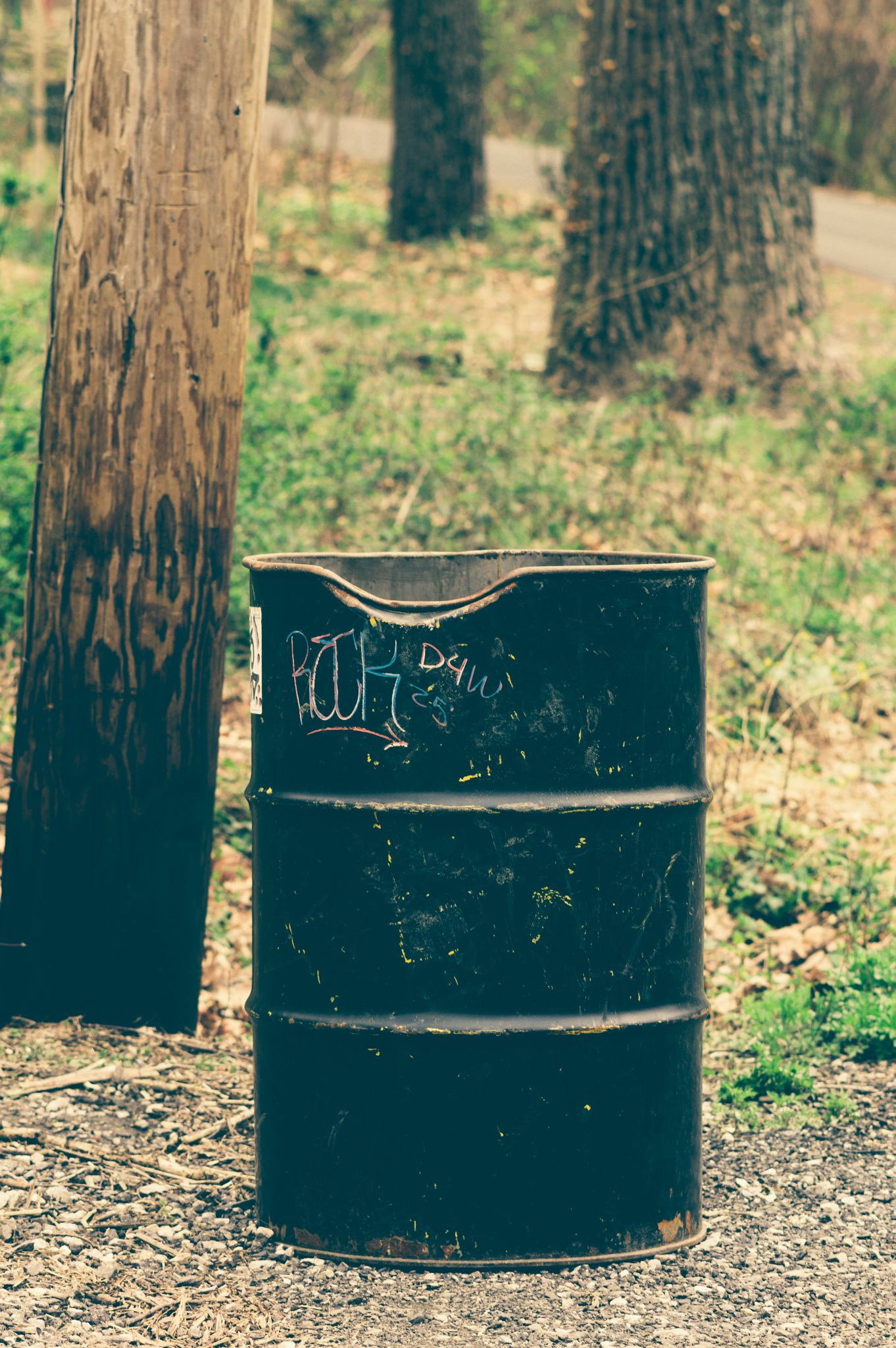 A black steel drum with graffiti on it next to a telephone pole along a trail